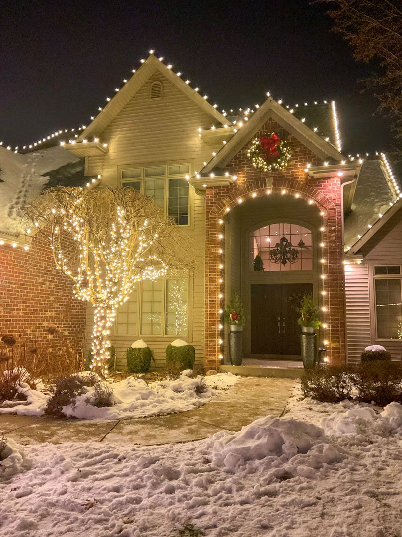 Warm white lights around a front entrance with a wreath and light-wrapped tree