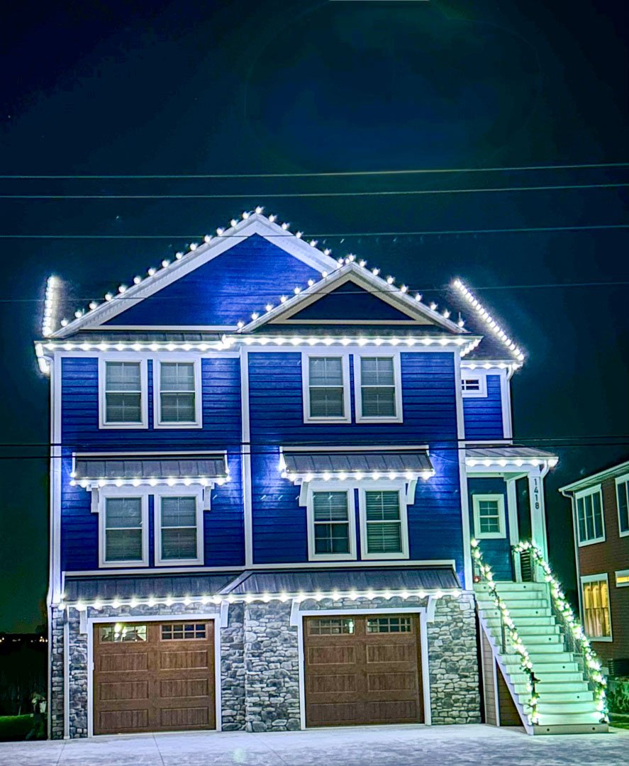 White roofline and window lights on a blue three-story home at night