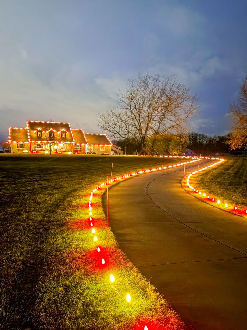 A curved driveway outlined with colorful lights leading to an illuminated home