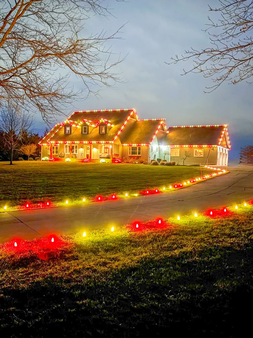 Colorful Christmas lights bordering a driveway and decorating a home